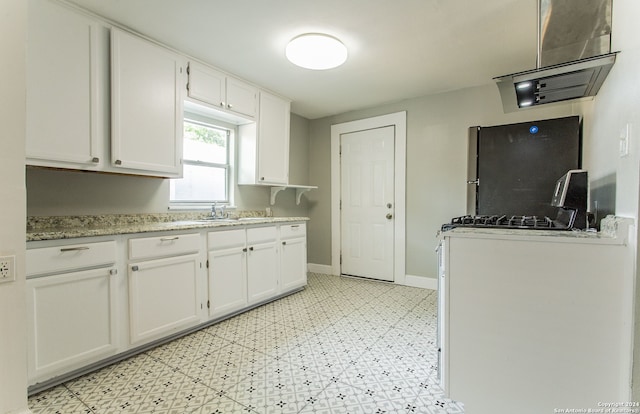 kitchen featuring stone countertops, stainless steel fridge, white cabinetry, and sink