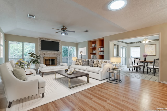 living room featuring ceiling fan, a textured ceiling, a fireplace, built in features, and light wood-type flooring