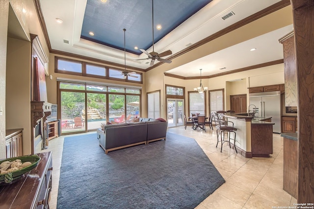 tiled living room with ornamental molding, a towering ceiling, ceiling fan with notable chandelier, and a tray ceiling