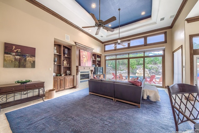 living room featuring a high ceiling, ornamental molding, ceiling fan, a tray ceiling, and a premium fireplace