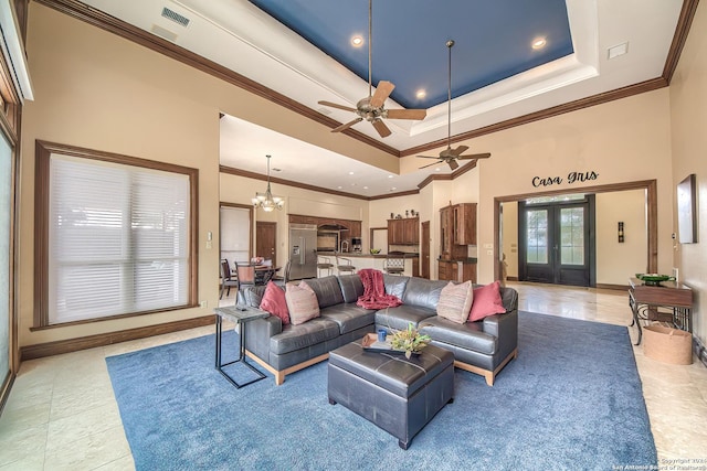 living room with ceiling fan with notable chandelier, a high ceiling, ornamental molding, a tray ceiling, and french doors