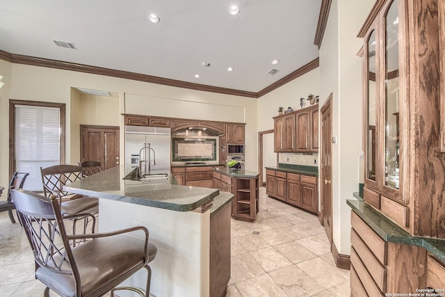 kitchen with crown molding, a breakfast bar area, built in appliances, tasteful backsplash, and an island with sink