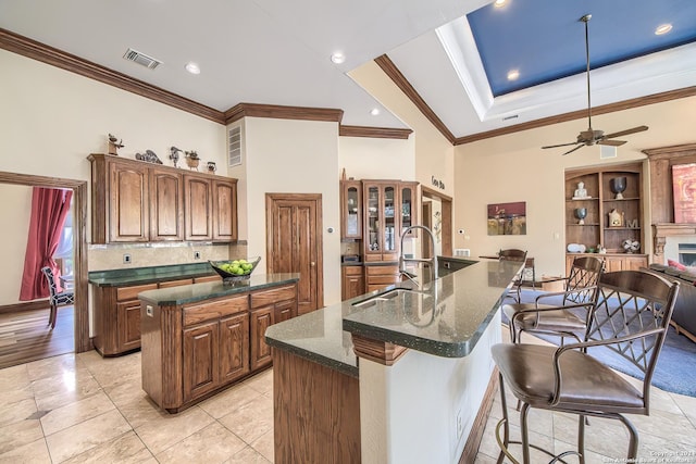 kitchen with a kitchen island with sink, sink, crown molding, and tasteful backsplash