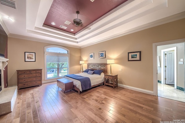 bedroom featuring ornamental molding, a raised ceiling, and light wood-type flooring