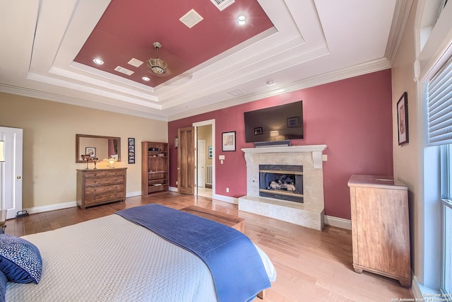 bedroom featuring a raised ceiling, crown molding, hardwood / wood-style floors, and a fireplace