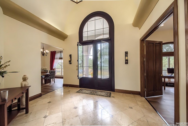 entryway with a towering ceiling, light tile patterned floors, an inviting chandelier, and french doors