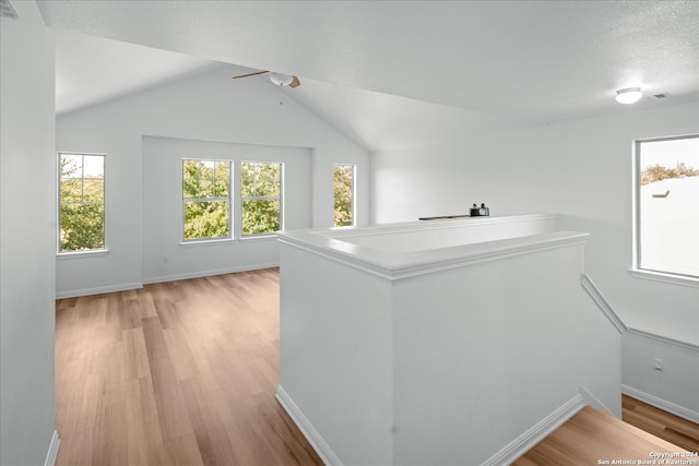 hall with light wood-type flooring, a textured ceiling, and vaulted ceiling