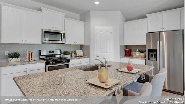 kitchen with stainless steel appliances, decorative backsplash, sink, an island with sink, and white cabinets