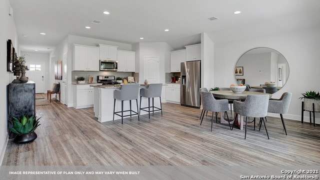 kitchen featuring stainless steel appliances, white cabinetry, an island with sink, a breakfast bar, and light hardwood / wood-style flooring