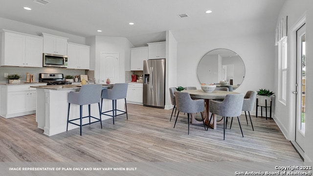 kitchen featuring white cabinetry, appliances with stainless steel finishes, tasteful backsplash, a kitchen island with sink, and light hardwood / wood-style flooring