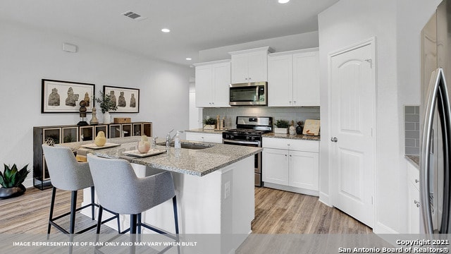 kitchen with light stone counters, a center island with sink, stainless steel appliances, white cabinetry, and sink