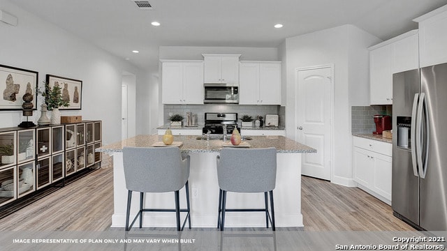 kitchen featuring white cabinets, a kitchen island with sink, light stone counters, and stainless steel appliances