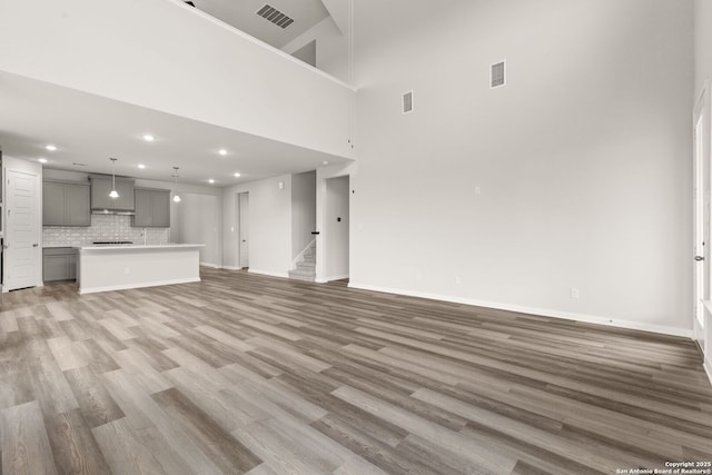 unfurnished living room with stairway, light wood-style flooring, visible vents, and baseboards