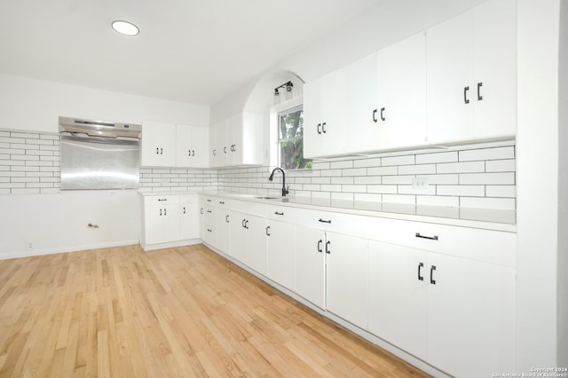 kitchen featuring sink, backsplash, white cabinetry, light wood-type flooring, and range hood