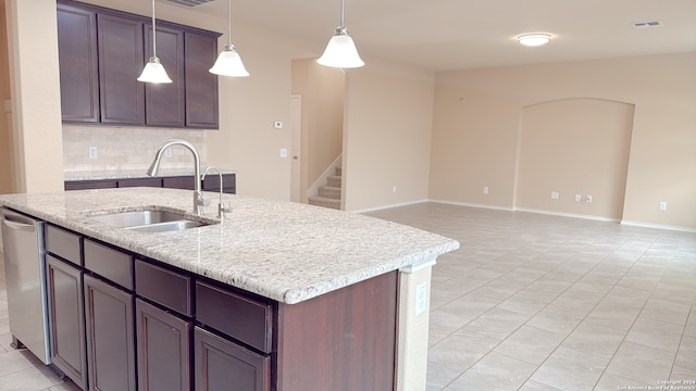 kitchen featuring dark brown cabinetry, sink, light stone counters, tasteful backsplash, and a kitchen island with sink