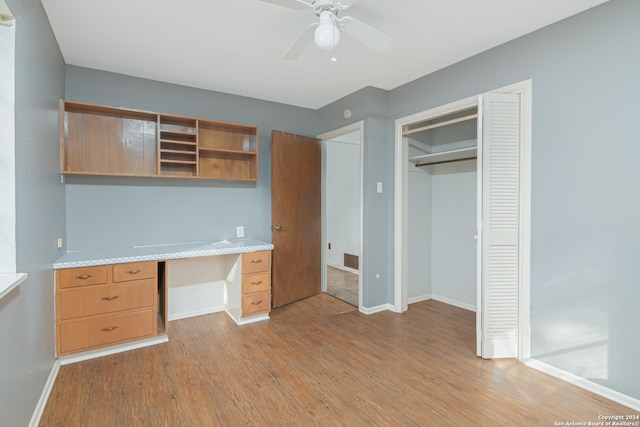 unfurnished office featuring light wood-type flooring, built in desk, and ceiling fan