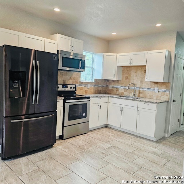 kitchen featuring light stone counters, backsplash, white cabinetry, appliances with stainless steel finishes, and sink