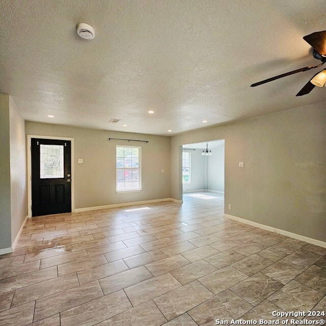 interior space featuring ceiling fan with notable chandelier and a textured ceiling