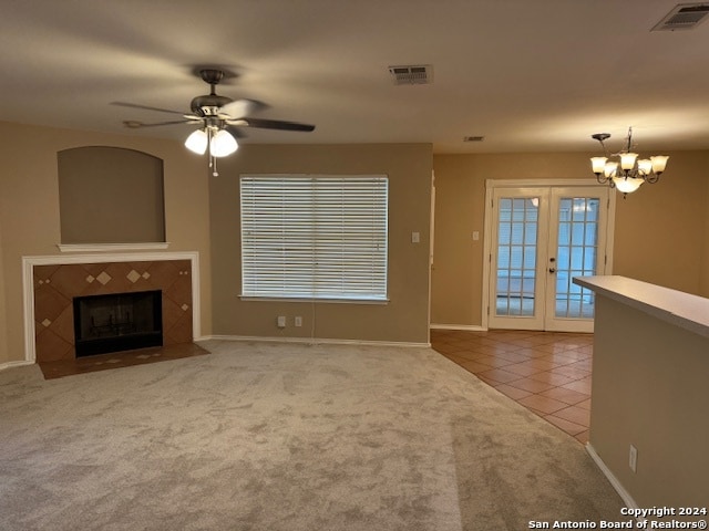 unfurnished living room featuring a fireplace, carpet, french doors, and ceiling fan with notable chandelier