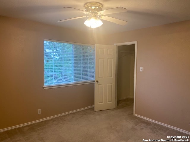 unfurnished bedroom with a walk in closet, carpet, ceiling fan, and a closet