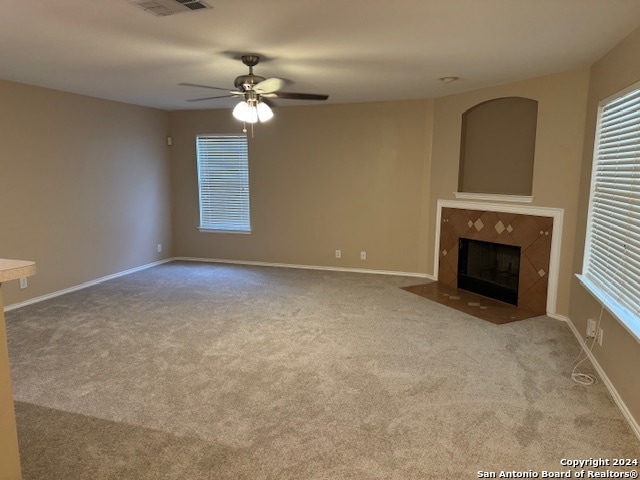 unfurnished living room with a tiled fireplace, light colored carpet, and ceiling fan