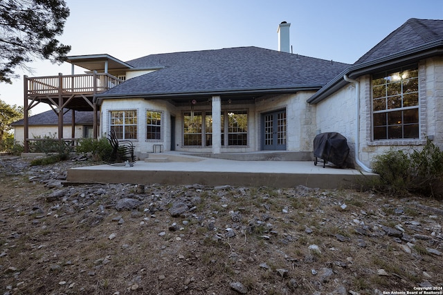 rear view of house featuring a patio, a deck, a chimney, and a shingled roof