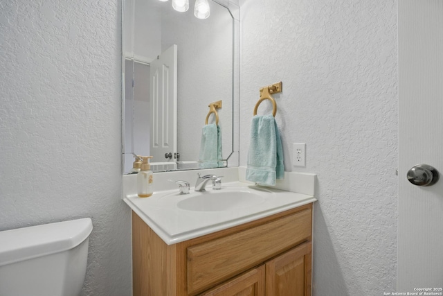 half bathroom featuring toilet, vanity, and a textured wall