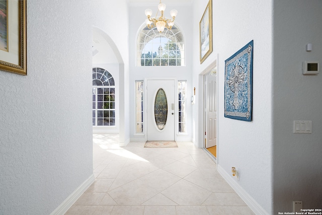 entryway with baseboards, an inviting chandelier, light tile patterned flooring, a towering ceiling, and a textured wall