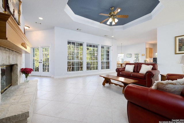 living area with a stone fireplace, a tray ceiling, light tile patterned flooring, and ceiling fan