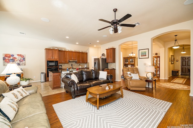 living room with light wood-type flooring and ceiling fan with notable chandelier