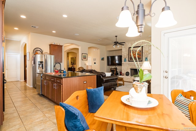 dining room with a fireplace, ceiling fan with notable chandelier, light tile patterned floors, and sink