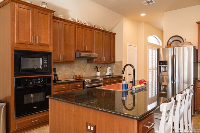 kitchen with black appliances, tasteful backsplash, dark stone counters, sink, and a kitchen island with sink