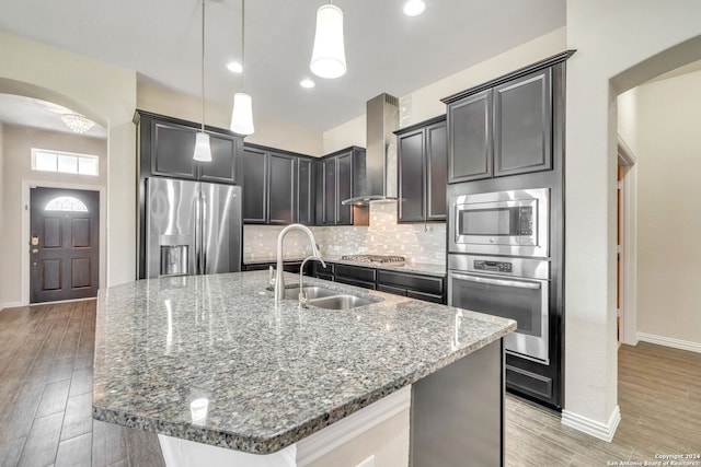 kitchen with stainless steel appliances, a center island with sink, hanging light fixtures, sink, and light wood-type flooring