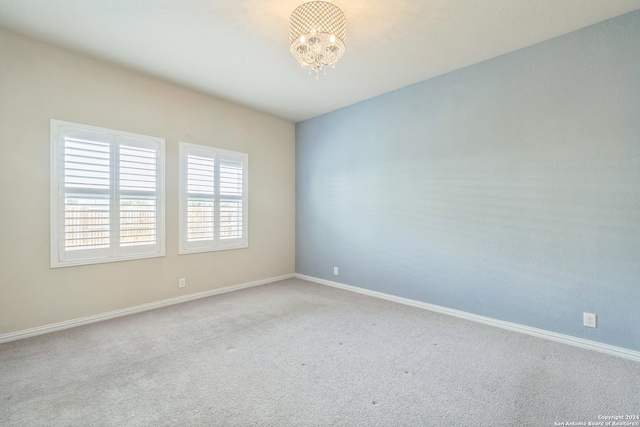 carpeted empty room featuring a notable chandelier