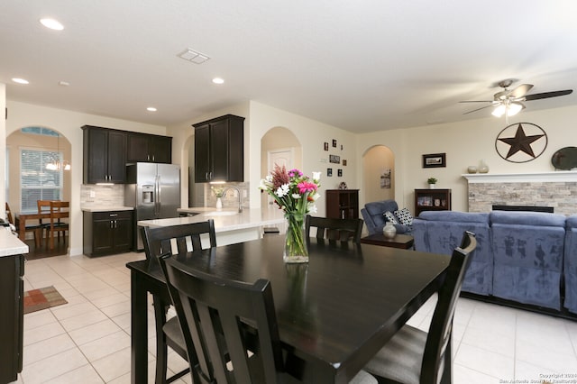 dining area featuring ceiling fan, a stone fireplace, and light tile patterned floors