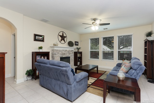 living room with ceiling fan, a stone fireplace, and light tile patterned floors