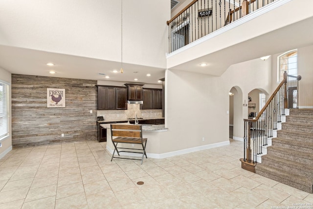 kitchen with light tile patterned flooring, dark brown cabinets, a kitchen bar, wooden walls, and a high ceiling