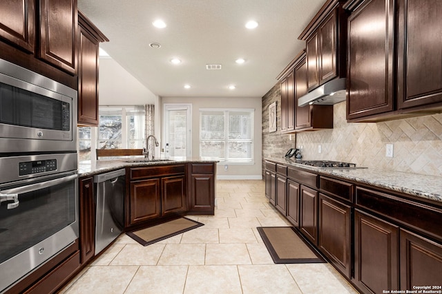 kitchen featuring backsplash, appliances with stainless steel finishes, light tile patterned floors, light stone countertops, and sink