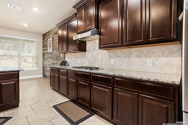 kitchen with dark brown cabinets, decorative backsplash, stainless steel gas stovetop, and light stone counters