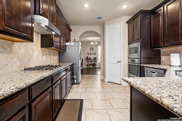 kitchen featuring light stone counters, a textured ceiling, light tile patterned flooring, backsplash, and appliances with stainless steel finishes