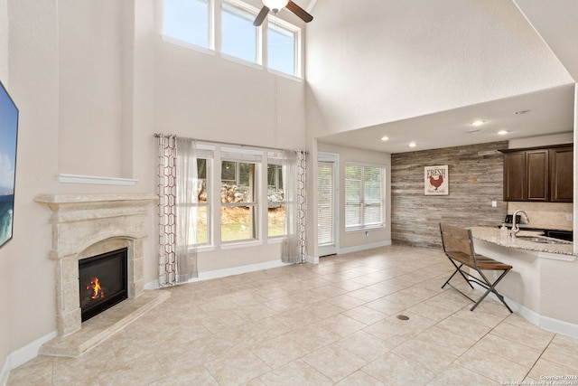 unfurnished living room with light tile patterned flooring, sink, ceiling fan, a towering ceiling, and a high end fireplace