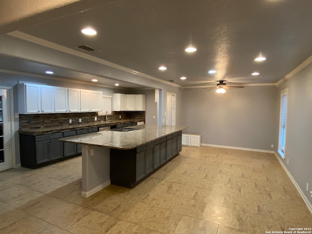 kitchen with tasteful backsplash, ornamental molding, white cabinetry, ceiling fan, and a center island