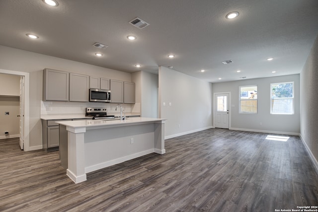 kitchen with dark wood-type flooring, gray cabinetry, an island with sink, and stainless steel appliances