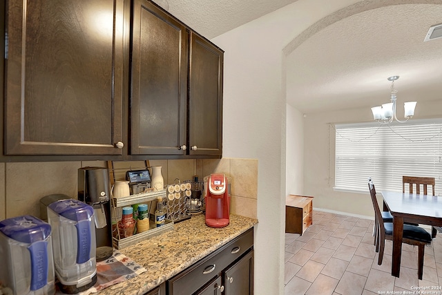 kitchen with dark brown cabinetry, a textured ceiling, pendant lighting, and light stone counters