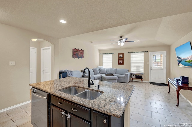 kitchen with light stone counters, a center island with sink, dark brown cabinetry, sink, and ceiling fan