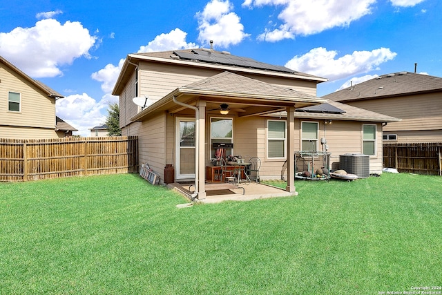 back of property with central AC unit, solar panels, ceiling fan, a patio, and a yard