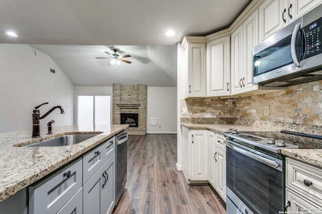 kitchen with sink, light stone counters, appliances with stainless steel finishes, dark wood-type flooring, and vaulted ceiling