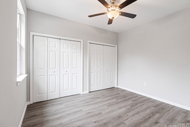 unfurnished bedroom featuring ceiling fan, multiple closets, and light hardwood / wood-style flooring