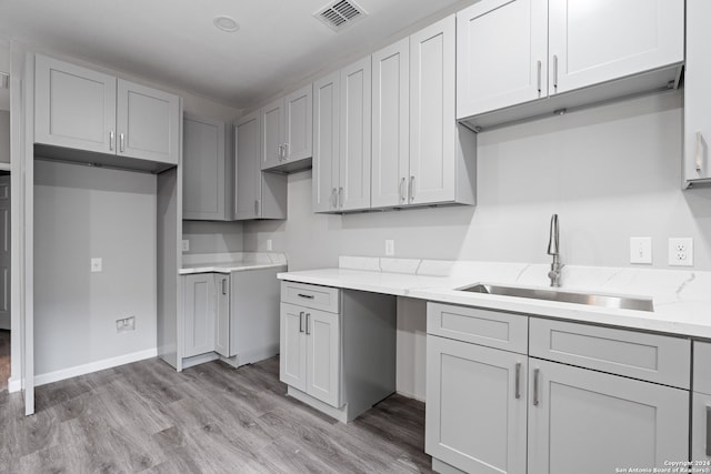 kitchen featuring gray cabinetry, light wood-type flooring, sink, and light stone countertops