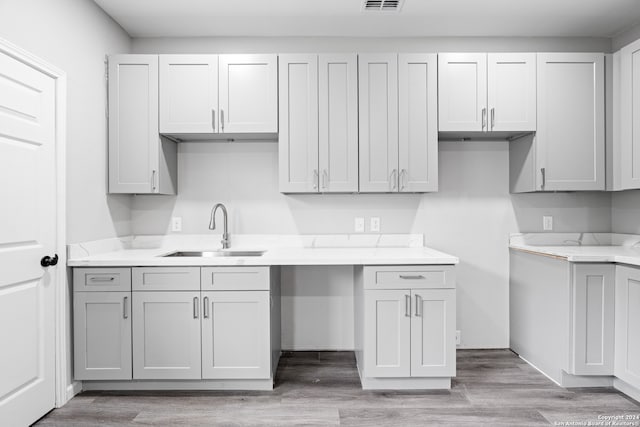 kitchen with gray cabinetry, light wood-type flooring, sink, and light stone counters